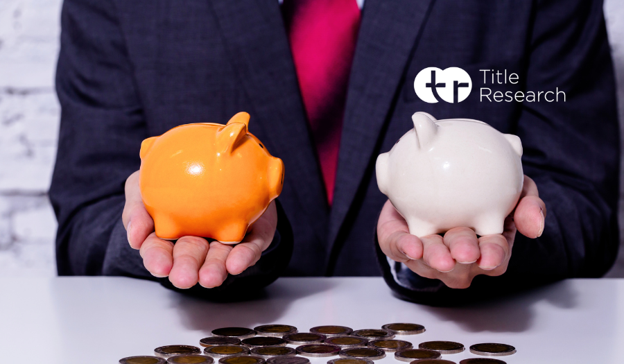 Man in a suit sitting at a desk with two different colour piggy banks and coins spread across the table