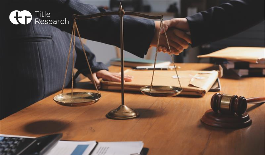 Two legal professionals shaking hands over a desk with the scales of justice on it
